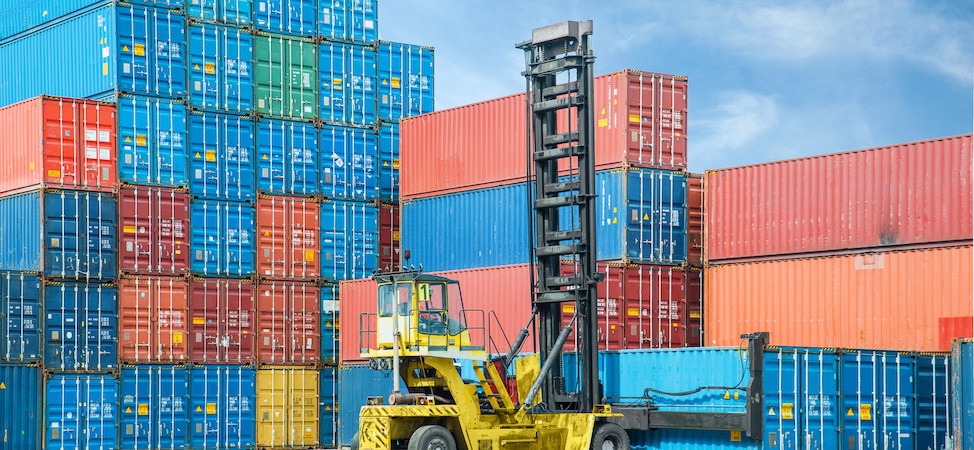 Forklift moving stacked shipping containers at port